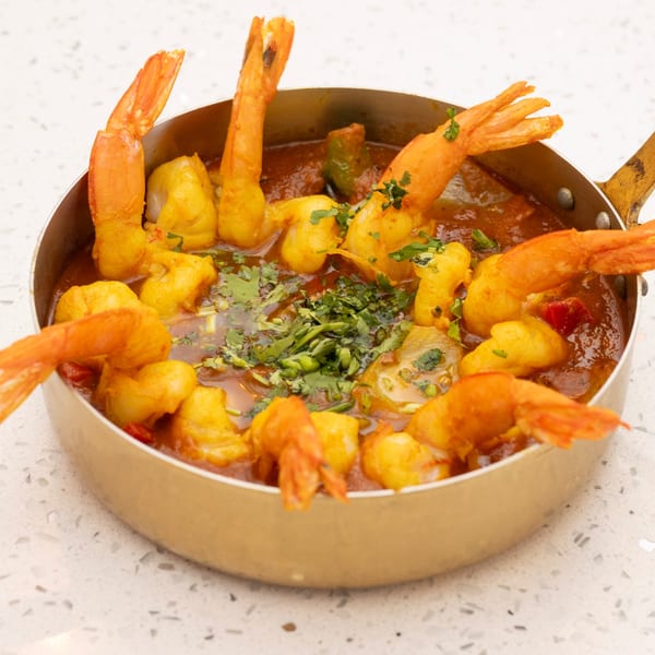 Shrimp and fish curry in a golden pan, garnished with fresh cilantro on a white countertop.