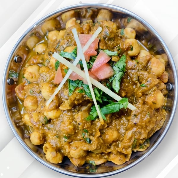 A close-up of Chana Masala, a chickpea curry, garnished with fresh cilantro, ginger, and tomatoes.