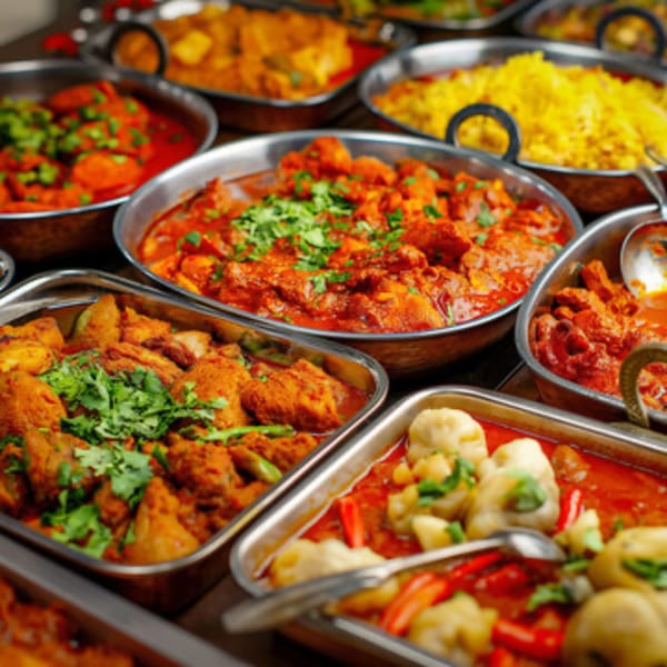 A buffet spread of various Indian dishes in metal serving bowls, including curries and yellow rice.