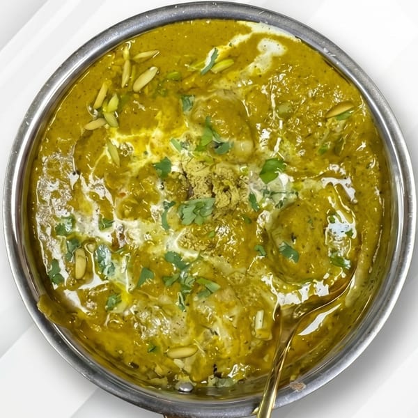 Overhead view of a vibrant green curry with cream swirls, nuts, and cilantro in a metal bowl.