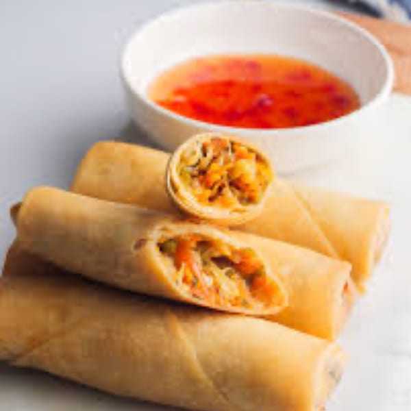 Golden spring rolls, one cut open to show vegetable filling, with a side of sweet chili sauce.