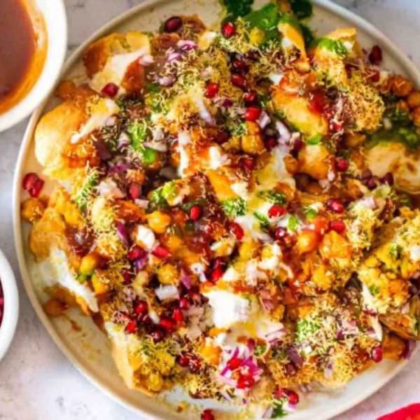 Close-up of a colorful Indian chaat dish with various toppings, including pomegranate seeds and sauces.