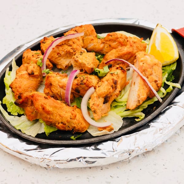 Sizzling chicken tikka with red onions, cilantro, and a lemon wedge on a bed of lettuce.