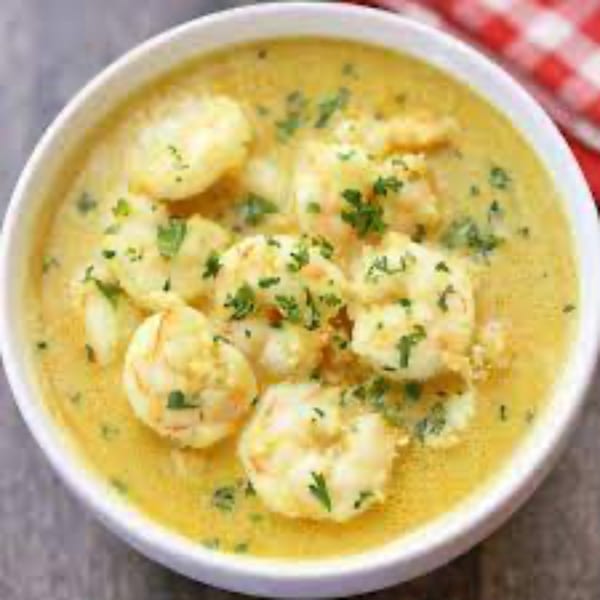 A white bowl filled with creamy yellow shrimp curry, garnished with fresh green herbs.