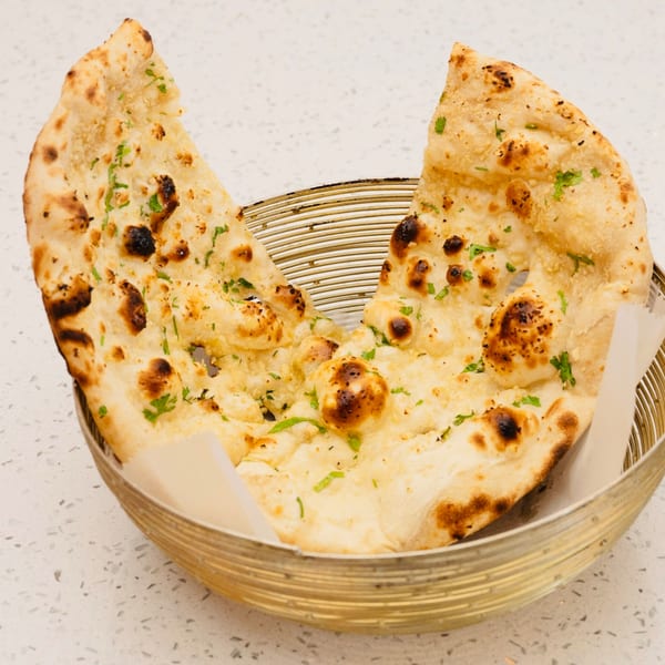 Two pieces of golden-brown naan bread, garnished with green herbs, in a gold wire basket.