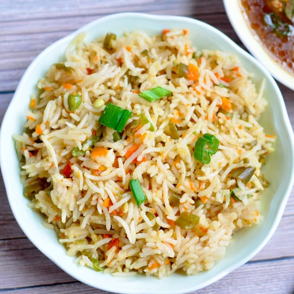Close-up of vegetable fried rice with carrots, peas, and green onions in a white bowl.