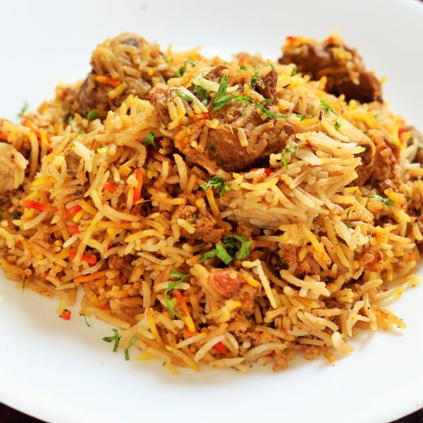 Close-up of a plate of chicken biryani, garnished with fresh green herbs.