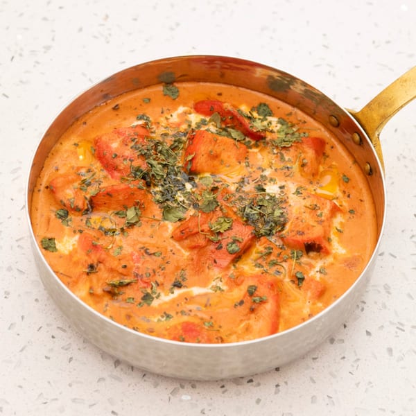 A copper pan filled with vibrant orange chicken tikka masala, garnished with fresh herbs.