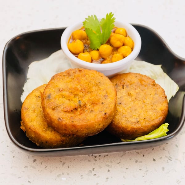 Three golden-brown potato patties with a side of chickpea curry and cilantro on a black plate.